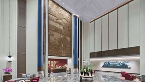 Een ruime lobby met een receptiebalie, een zithoek en een decoratieve muurschildering.
