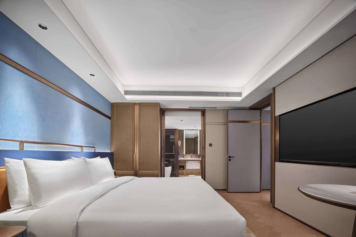 Une chambre d’hôtel avec un grand lit, une télévision, une armoire et une salle de bain visible à travers une porte ouverte.