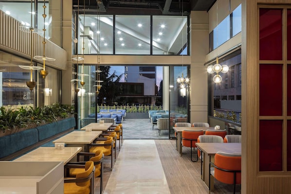 A modern indoor dining area with multiple tables and chairs, large windows, and a view of the outside. - Doubletree By Hilton Suites Trabzon Yomra (Yomra)