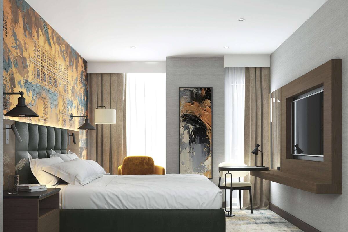 A modern hotel room with a large bed, a desk, and a comfortable armchair.