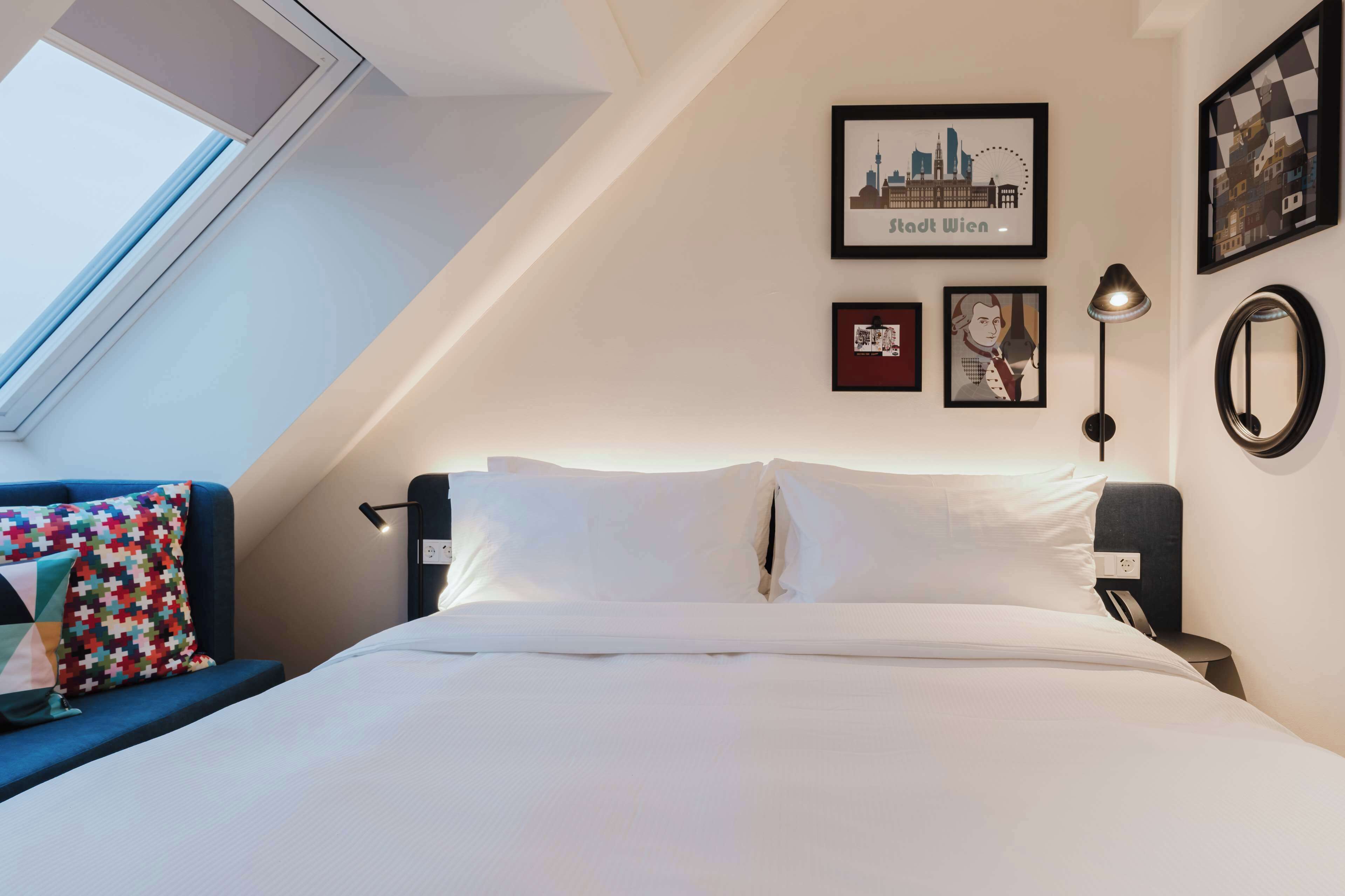 Una habitación de hotel con una cama, una ventana, una fotografía de la ciudad y una obra de arte enmarcada en la pared.