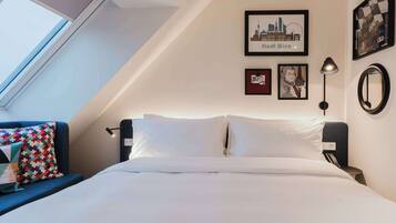 Quarto de hotel com uma cama, uma janela, uma pintura de paisagem urbana e uma obra de arte emoldurada na parede.