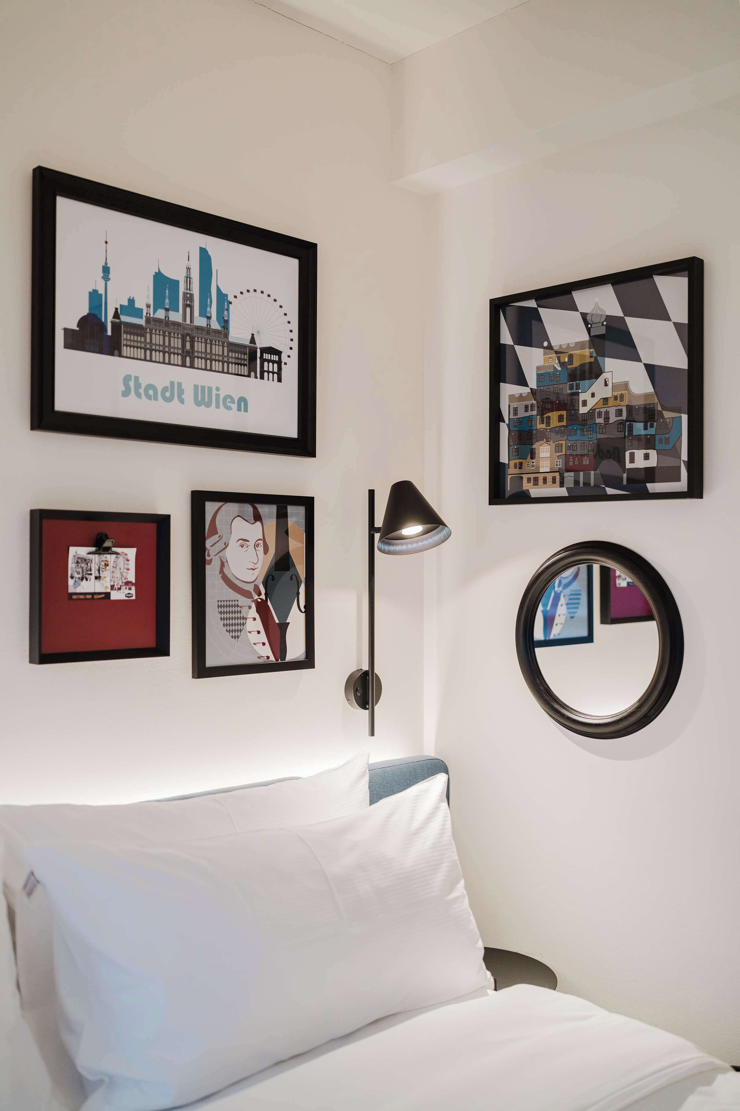 Habitación de hotel con una cama, una vista enmarcada de Viena, un retrato enmarcado, una lámpara y un espejo redondo.