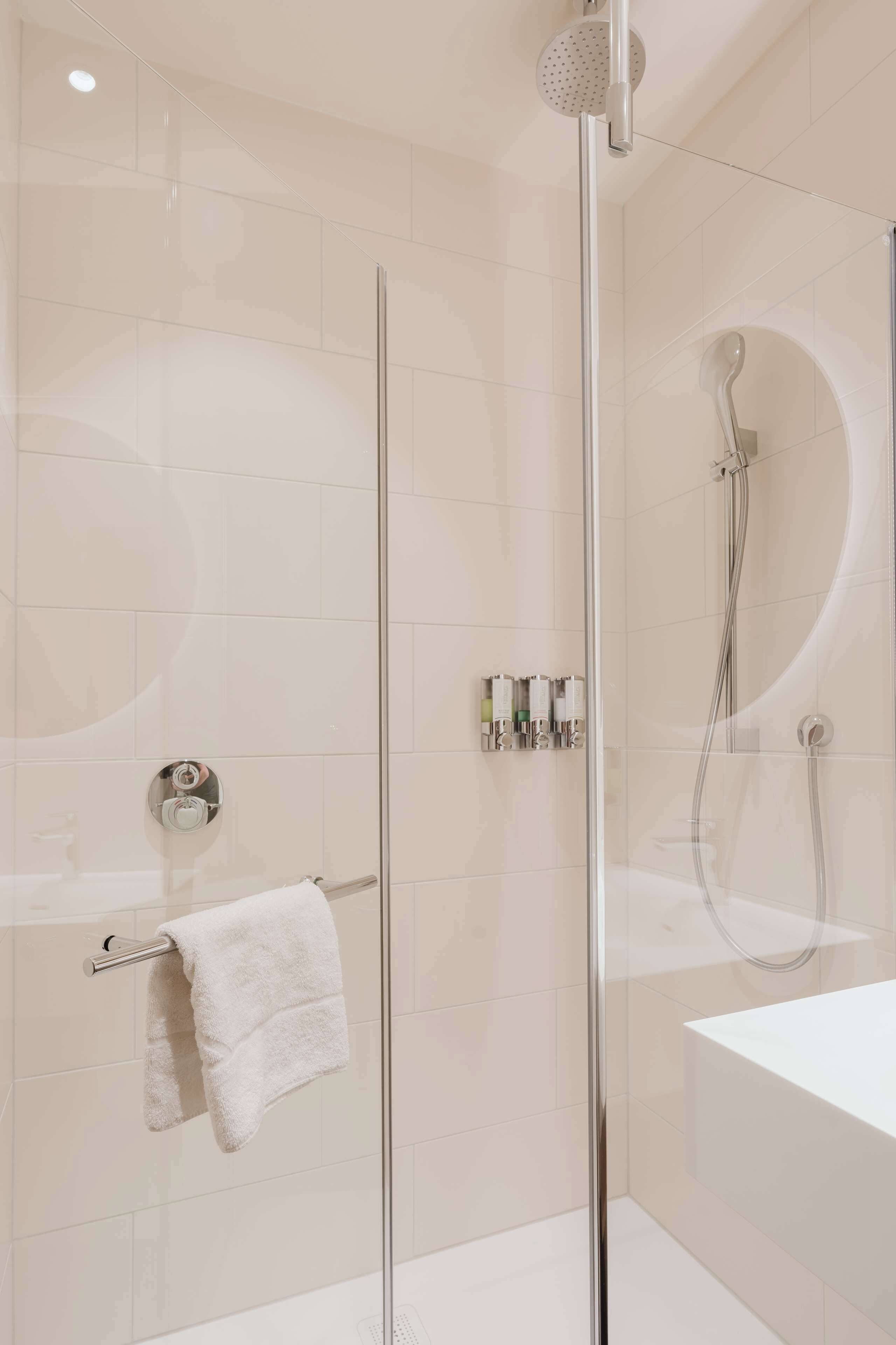 Un baño moderno con ducha envuelta en vidrio, una bañera blanca y un perchero para toallas.