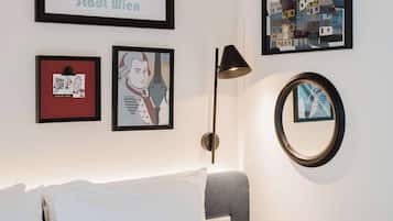 Habitació d'hotel amb un llit, una làmpada de paret i obra d'art emmarcada, incloent una vista urbana i un retrat.