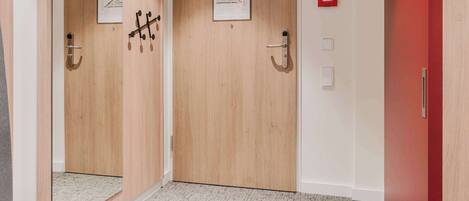 Un pasillo de hotel con puertas de madera, una puerta roja y suelo alfombrado.