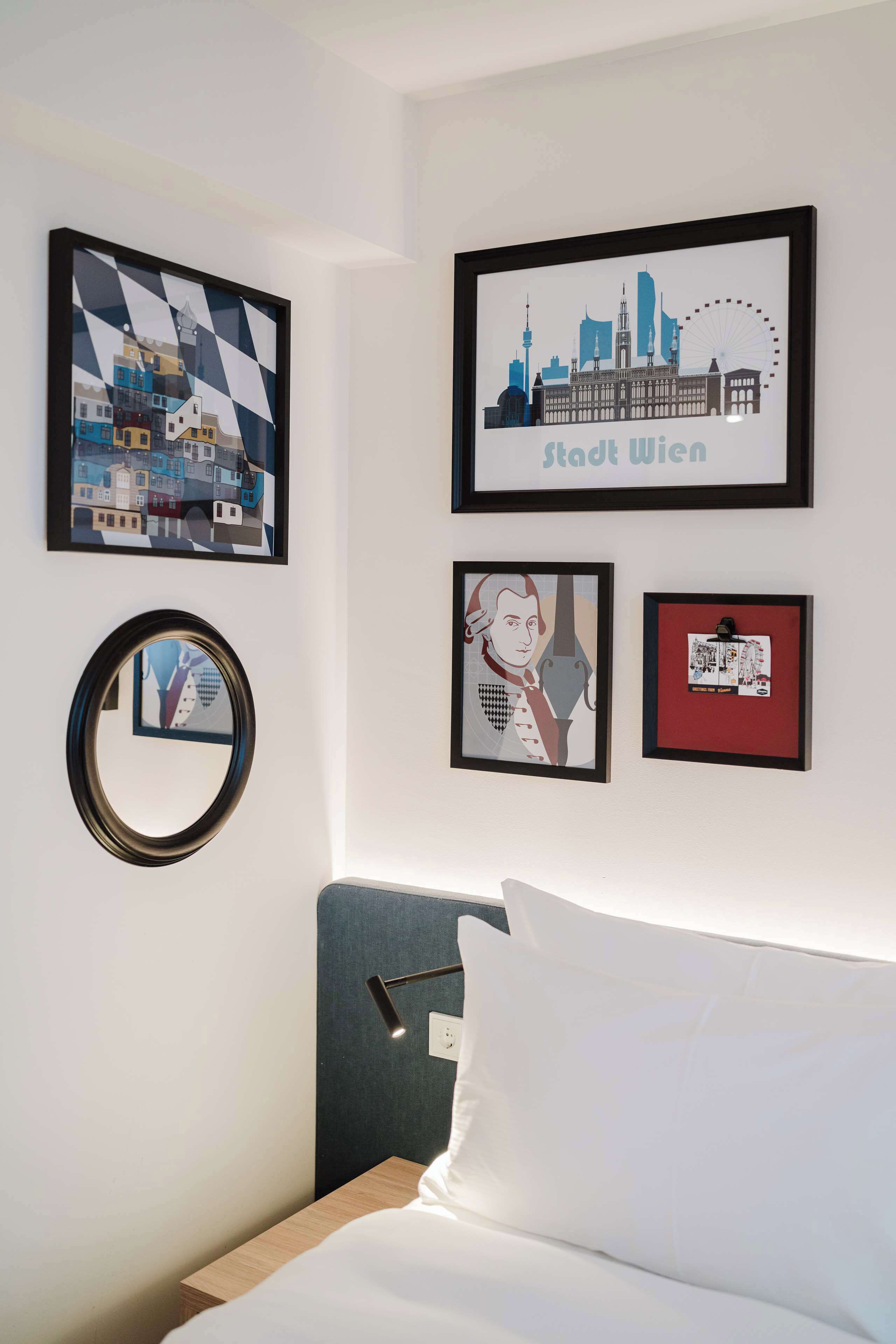 Quarto de hotel com cama, espelho redondo e três quadros na parede.