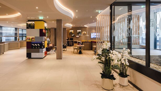 En moderne hotellobby med receptionsdisk, siddeområde og dekorative planter.