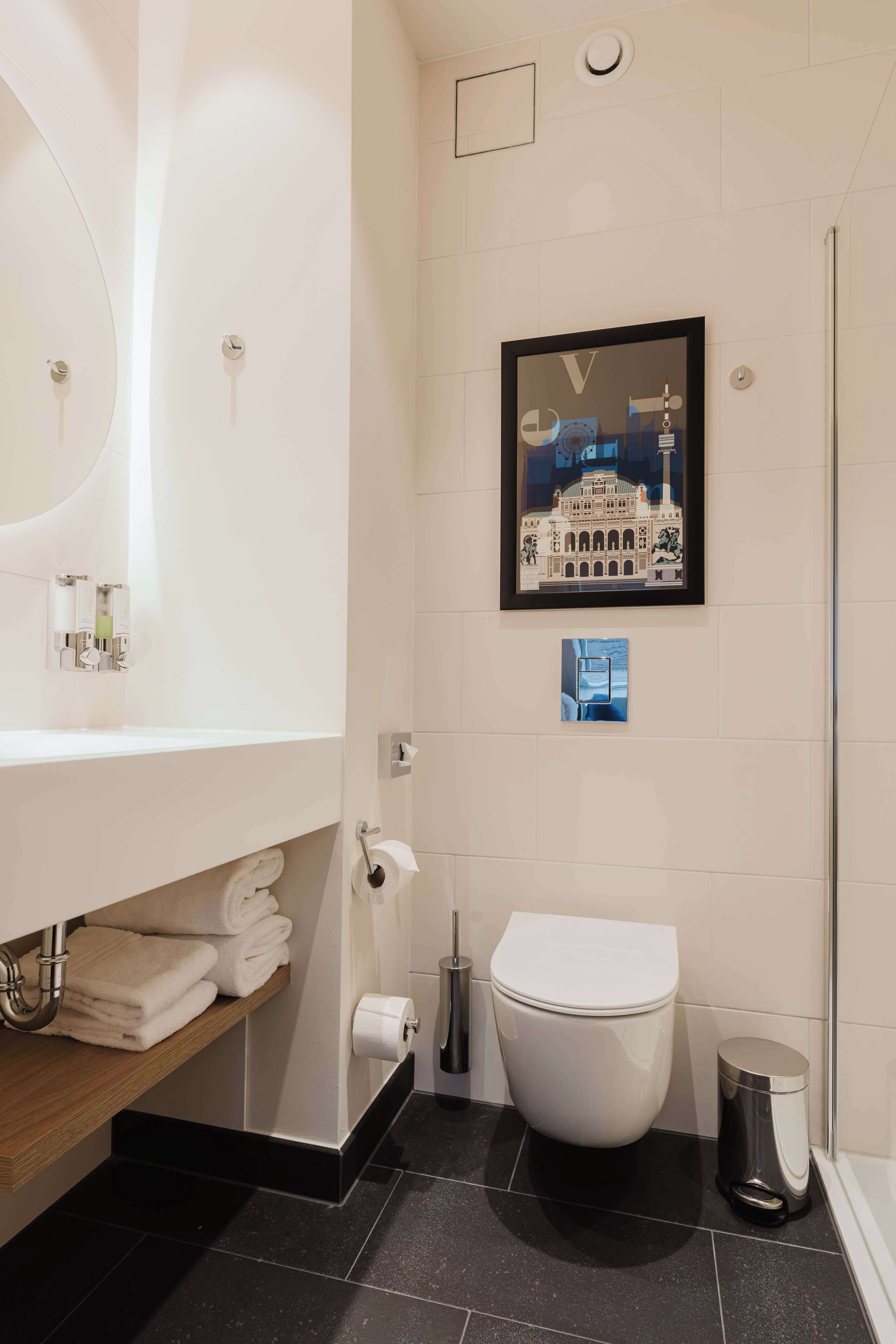 Une salle de bain moderne avec des toilettes blanches, un lavabo avec un miroir et un tableau encadré au mur.