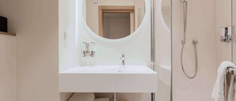 A modern bathroom with a round mirror, white sink, and glass-enclosed shower.