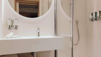 A modern bathroom with a white sink, a round mirror, a glass-enclosed shower, and a towel rack.
