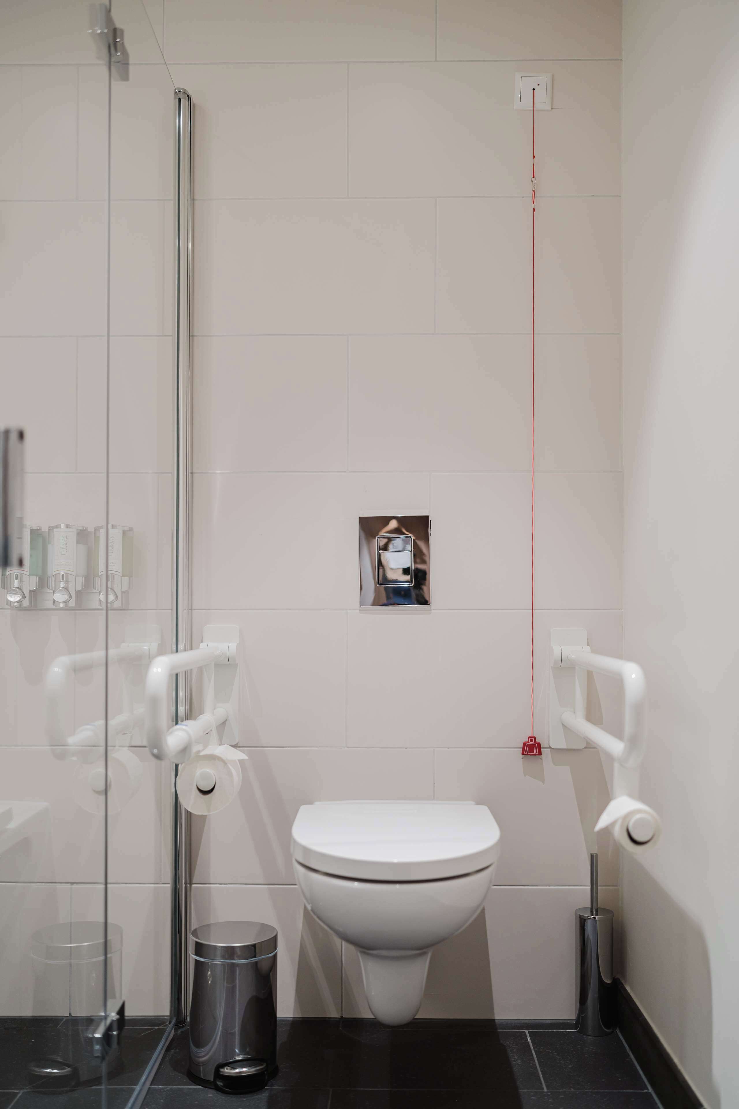 A modern bathroom with a glass shower enclosure, a white toilet, and a trash bin.
