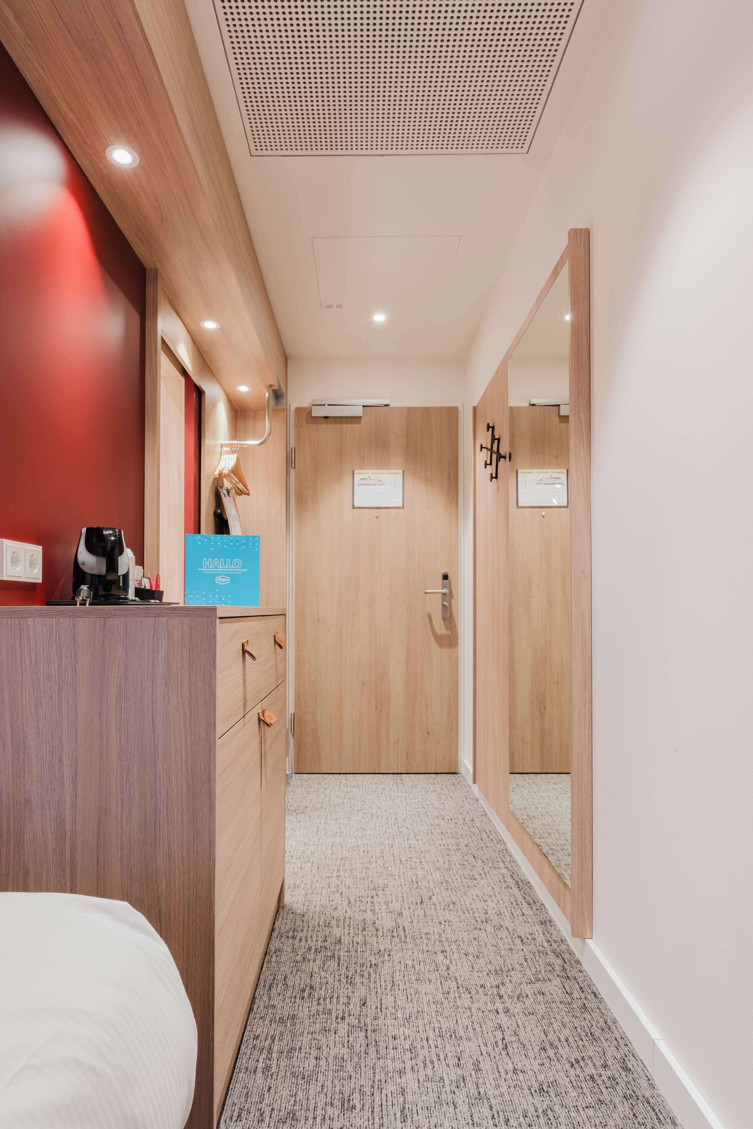 A hotel room with a wooden desk, a bed, a mirror, and a door leading to another room.