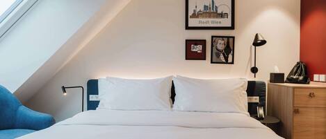 A hotel room with a bed, a desk, a chair, a lamp, a dresser, and framed pictures on the wall.