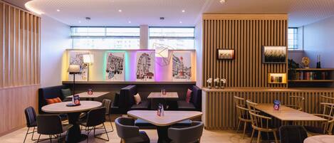 Un restaurante moderno con mesas redondas y cabinas, una pared decorativa de madera y obras de arte en la pared de fondo.