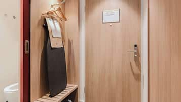 Un vestiaire en bois avec un banc, un portant à vêtements et une porte sur laquelle est apposée une pancarte.