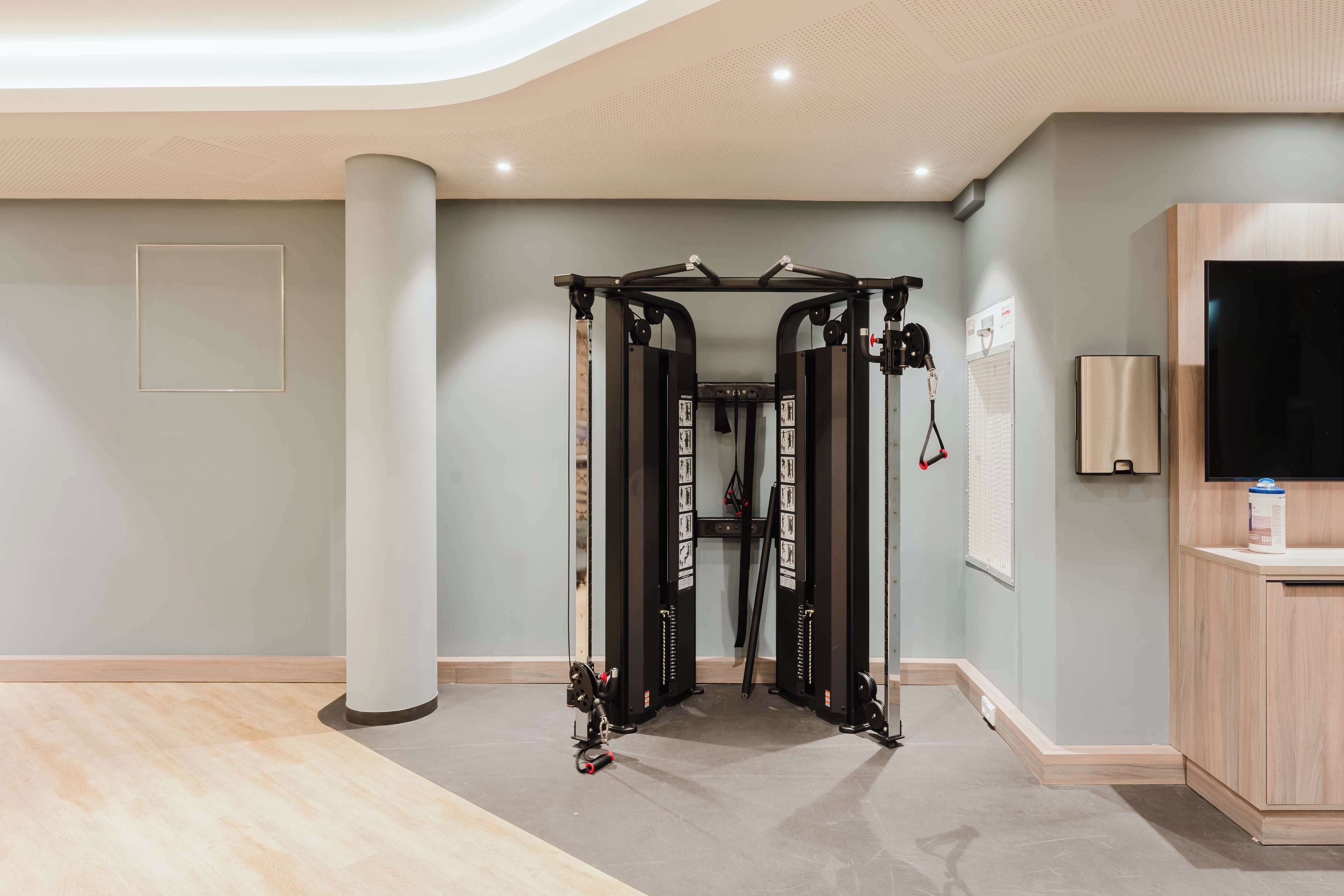 Une salle de sport moderne équipée d’une barre de traction, d’un grand pilier et d’un meuble en bois avec un téléviseur.