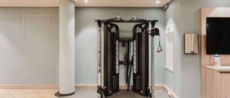 Une salle de sport moderne équipée d’une barre de traction, d’un grand pilier et d’un meuble en bois avec un téléviseur.