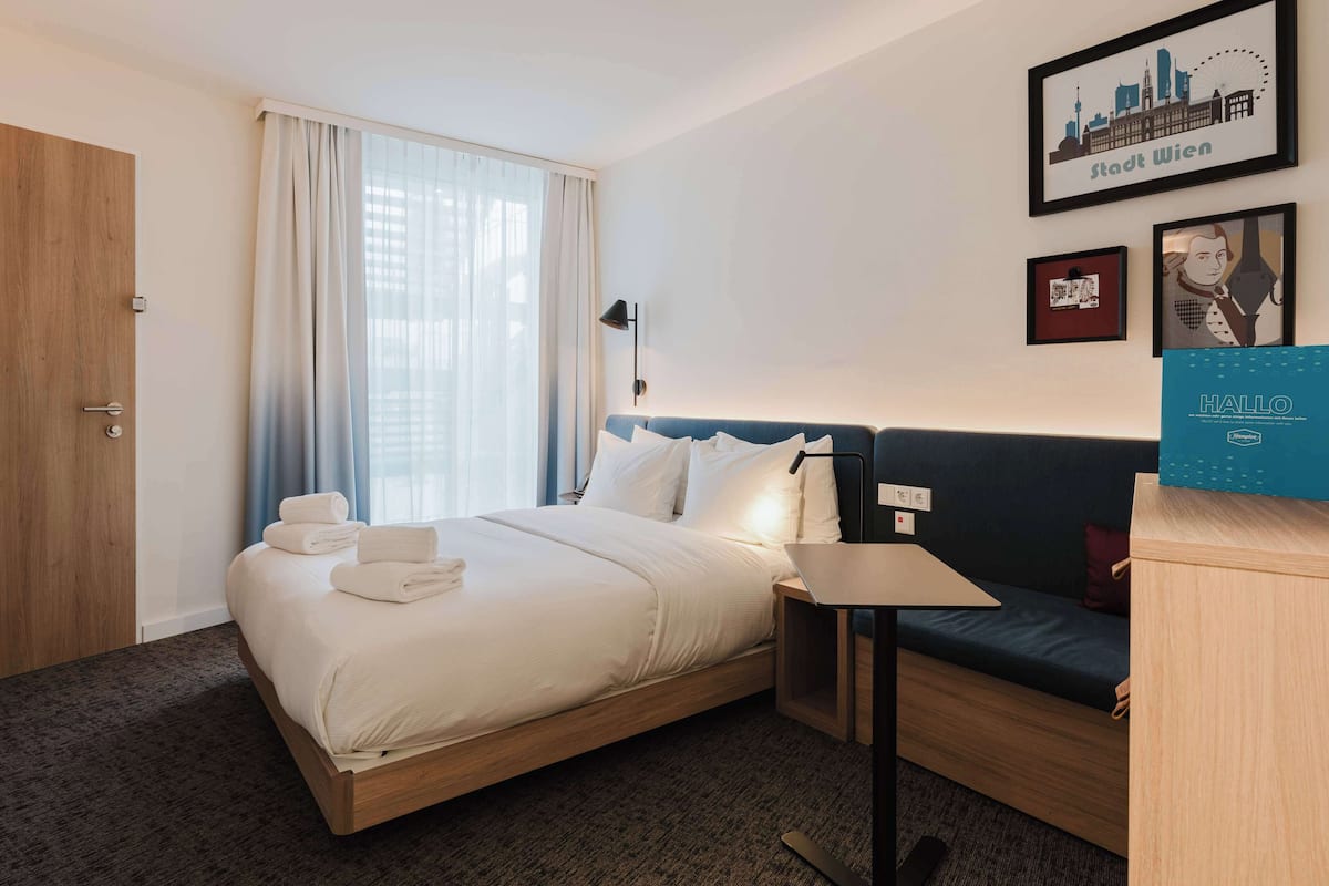 Une chambre d’hôtel avec un lit, un canapé, un bureau et un tableau représentant un paysage urbain accroché au mur.