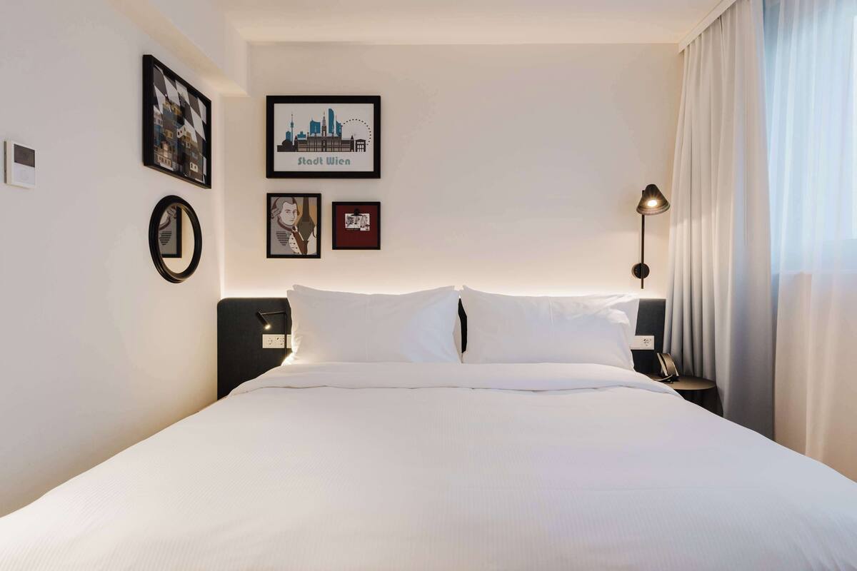 Une chambre d’hôtel avec un lit bien fait, une table de chevet avec une lampe et des tableaux encadrés au mur.