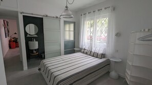 A bedroom with a bed, a bedside table, a mirror, a wardrobe, and a window with curtains.