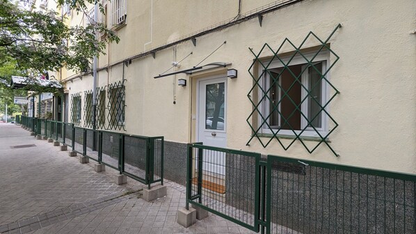 A building with a green metal fence, a door with a window, and a sign above the door.