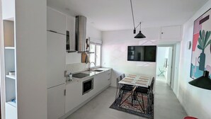 A modern kitchen with white cabinetry, a built-in oven, a sink, and a dining area with a table and chairs. - Madrid Mola ! (Madrid)