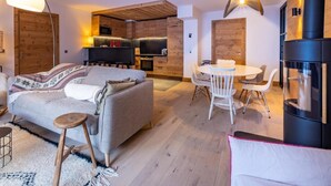 A modern living room with a sofa, a dining table, and chairs. There is a kitchen area with a stove and cabinets. - 2nd floor, terrace, fireplace or stove, parking, tv, ski locker, 95m², Méribel-Mottaret (Méribel - Les Allues)