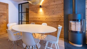 A modern interior with a round white table surrounded by white chairs, a wooden wall, and a black fireplace. - 2nd floor, terrace, fireplace or stove, parking, tv, ski locker, 95m², Méribel-Mottaret (Méribel - Les Allues)