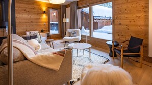 A cozy living room with a sofa, armchair, and coffee table, wooden walls, and a large window with a view of a snowy landscape. - 2nd floor, terrace, fireplace or stove, parking, tv, ski locker, 95m², Méribel-Mottaret (Méribel - Les Allues)