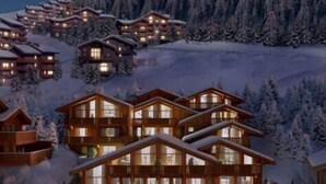 Un ensemble de bâtiments de style chalet, dotés de nombreux balcons, entourés d’arbres couverts de neige et se dressant sur un fond de montagnes.