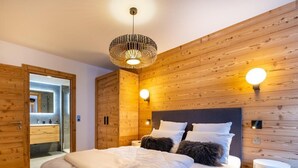 Une chambre moderne avec une tête de lit en bois, un grand lit avec une literie blanche, deux lampes de lecture fixées au mur et une table de chevet avec une lampe.