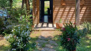 A wooden cabin with a covered entrance, surrounded by potted plants and trees. - Ecolodge calme & piscine privée (Roquetaillade-et-Conilhac)