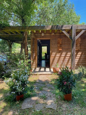 Een houten chalet met een overdekte ingang, omringd door potplanten en bomen.