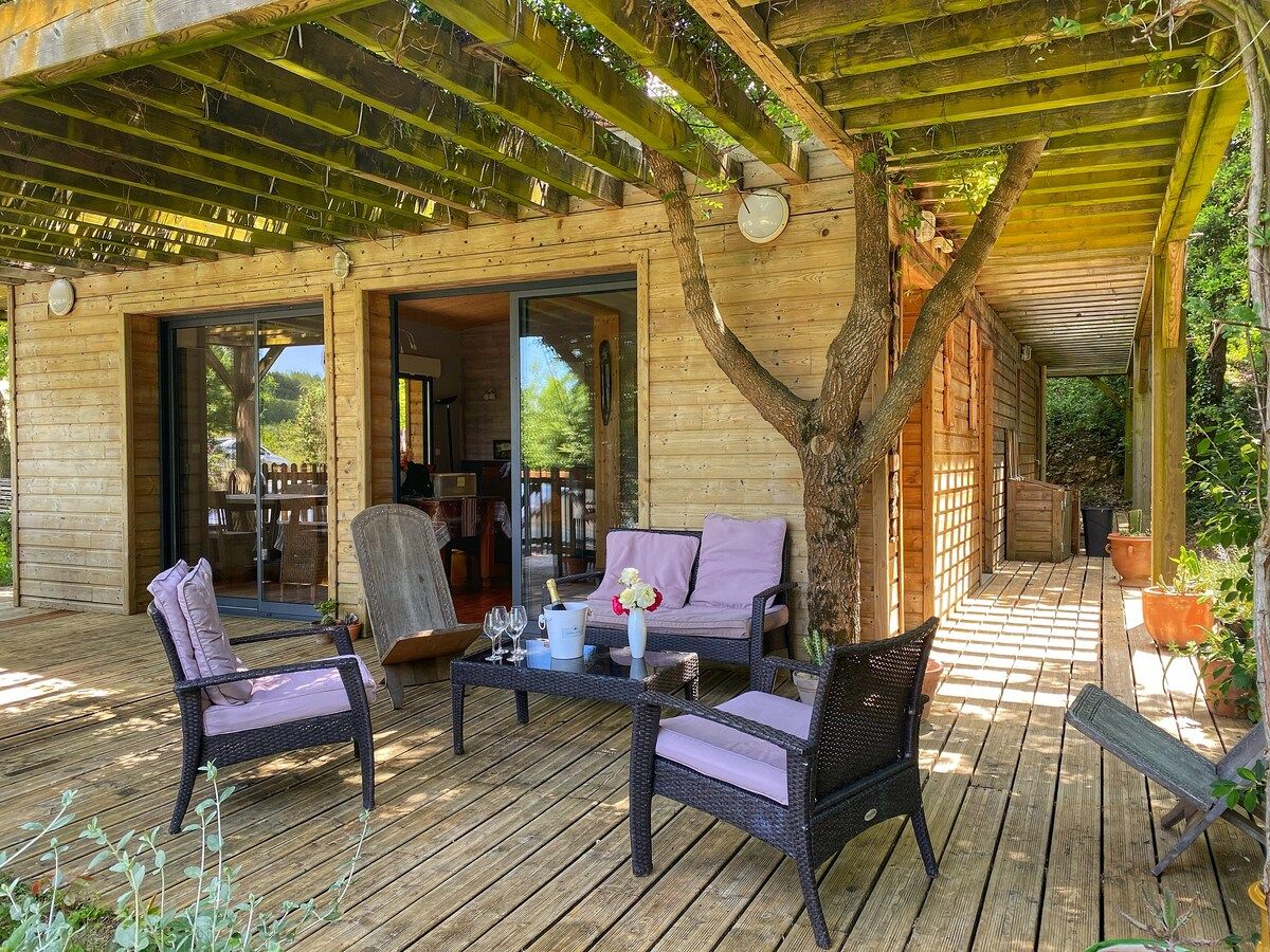 An outdoor wooden deck with wicker furniture, a glass door leading to an interior space, and potted plants.