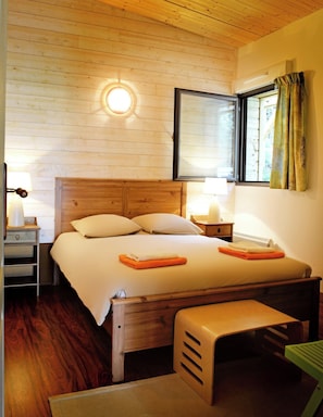 Een slaapkamer met een houten bed, nachtkastjes, een bankje, een raam met gordijnen en een wandlamp.