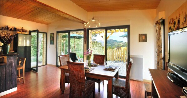 A dining area with a wooden table and chairs, a television, and a view of the outdoors.