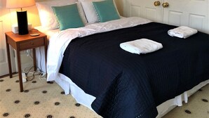Una cama bien hecha con edredón negro y ropa blanca, una mesita de noche con lámpara y una puerta con tirador de latón.