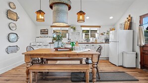 A spacious kitchen with a wooden dining table, pendant lights, and a view of the outdoors.