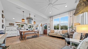 A spacious kitchen with a dining area, large windows, and a ceiling fan.
