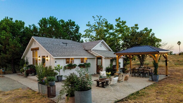 A house with a covered patio area, outdoor seating, and potted plants.