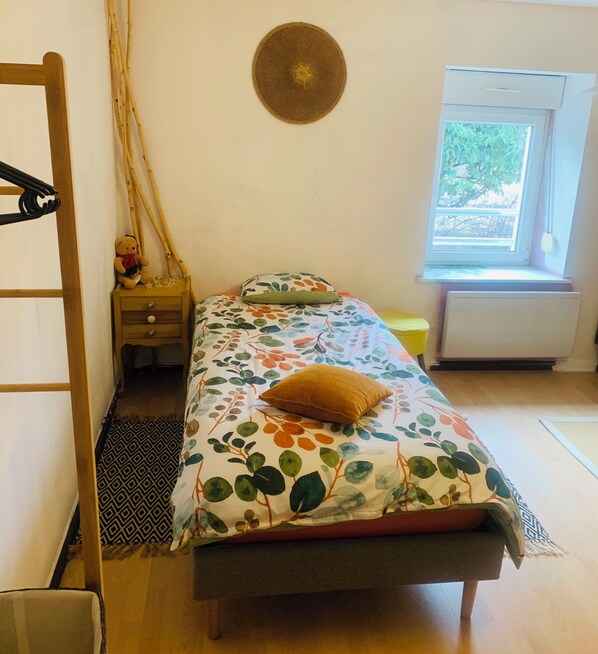 A small, cozy bedroom with a bed, a nightstand, a window, and a radiator.