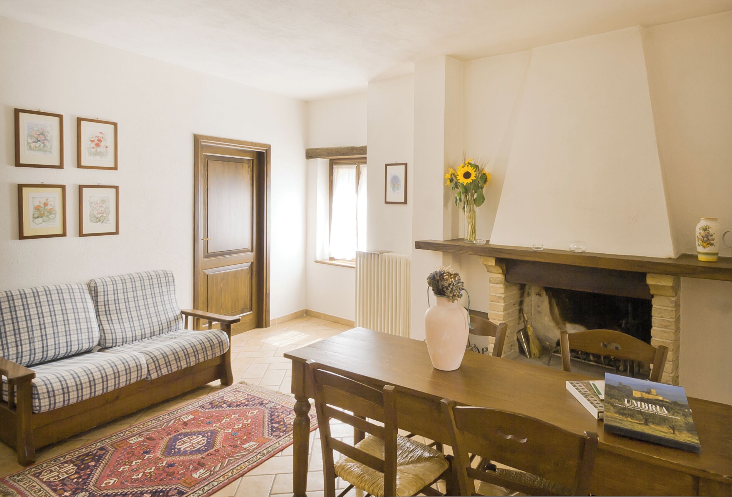 A living room with a sofa, a dining table, chairs, a fireplace, and framed pictures on the wall.