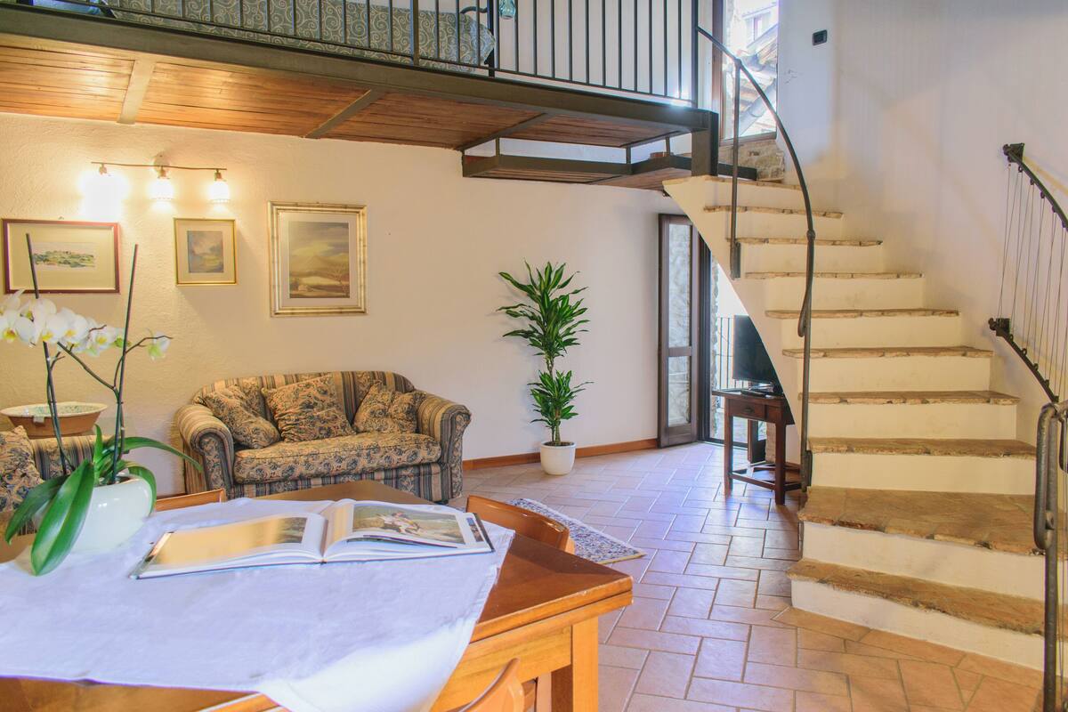 A spacious living area with a wooden staircase, a sofa, a dining table, and a potted plant.