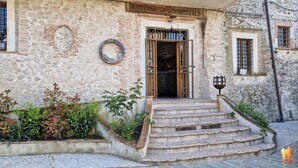 A stone building with a wooden door, steps leading up to the entrance, and a small garden area with plants. - Borgo San Valentino  (Arrone)