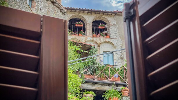 A stone building with arched windows and a balcony with potted plants. - Borgo San Valentino  (Arrone)