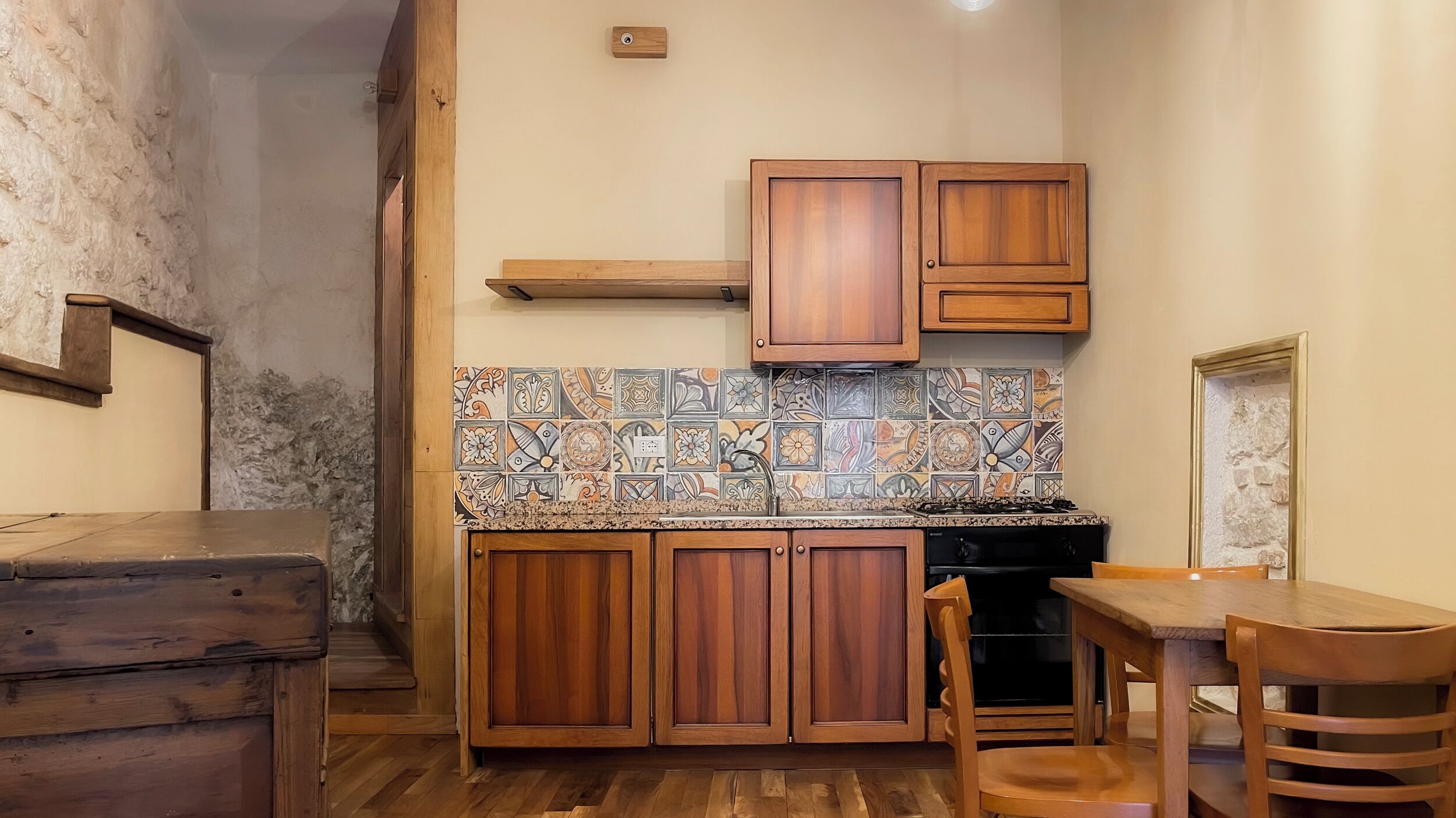 A compact kitchen with wooden cabinets, a tiled backsplash, and a dining area with a table and chairs.