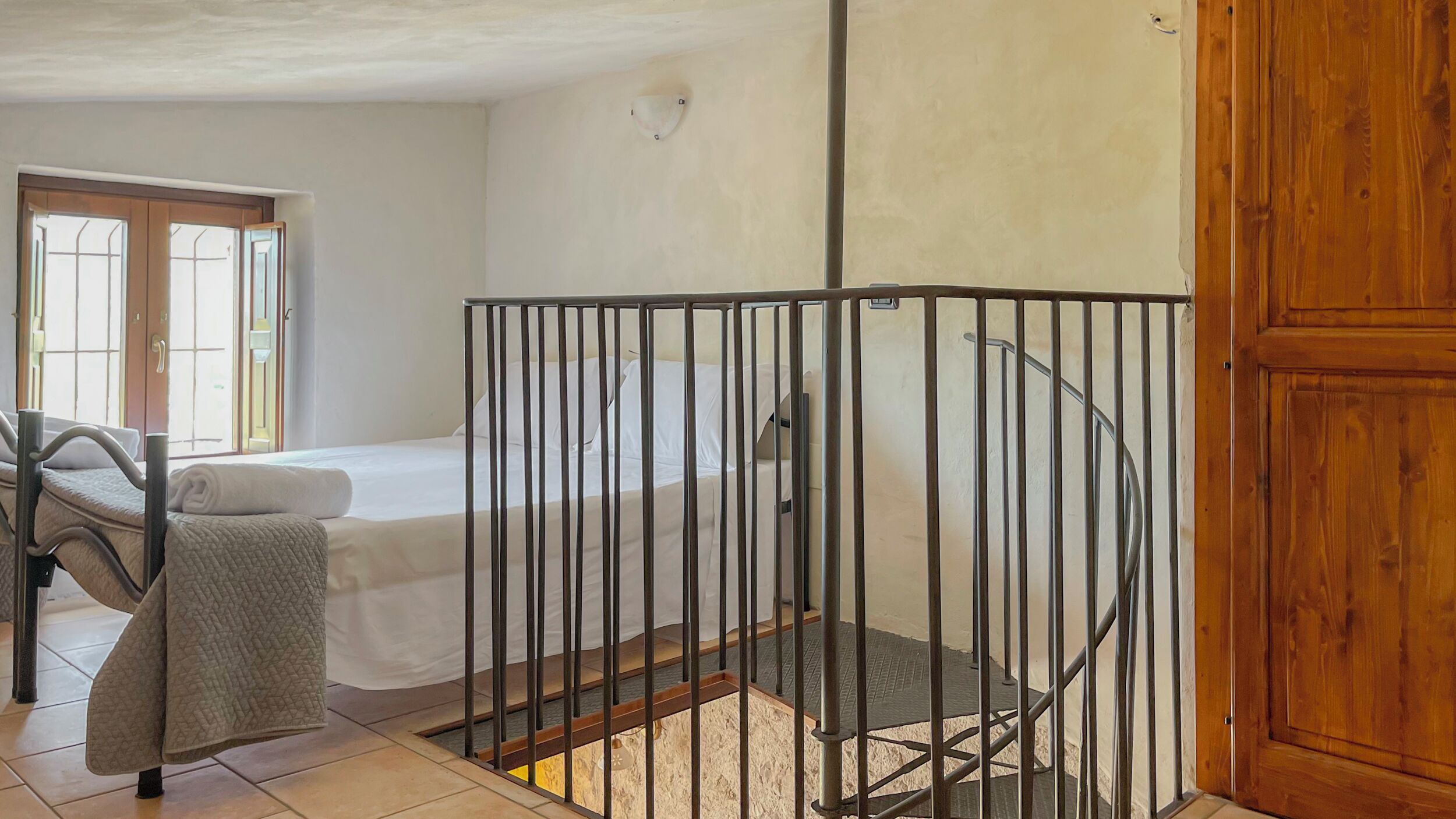 A room with a bed, a chair, a wooden door, and a metal gate.