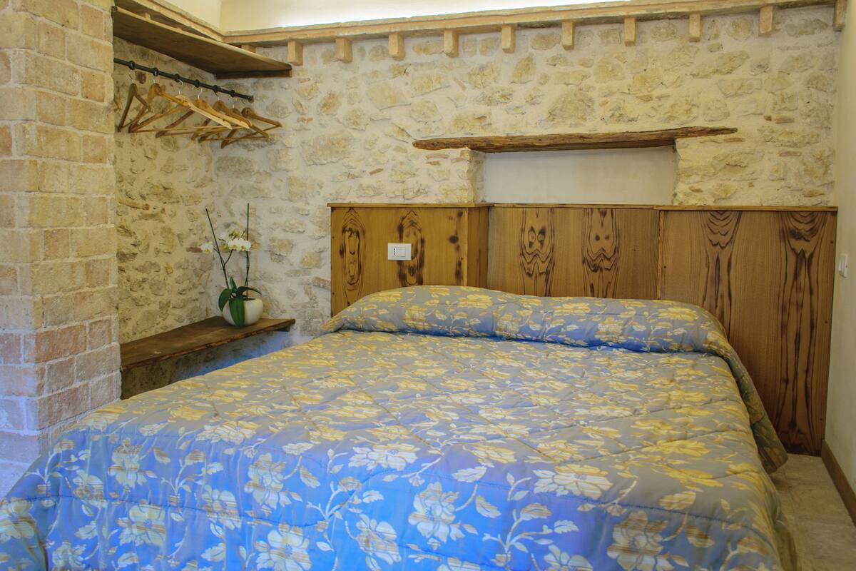 A bedroom with a stone wall, wooden headboard, and a floral bedspread.