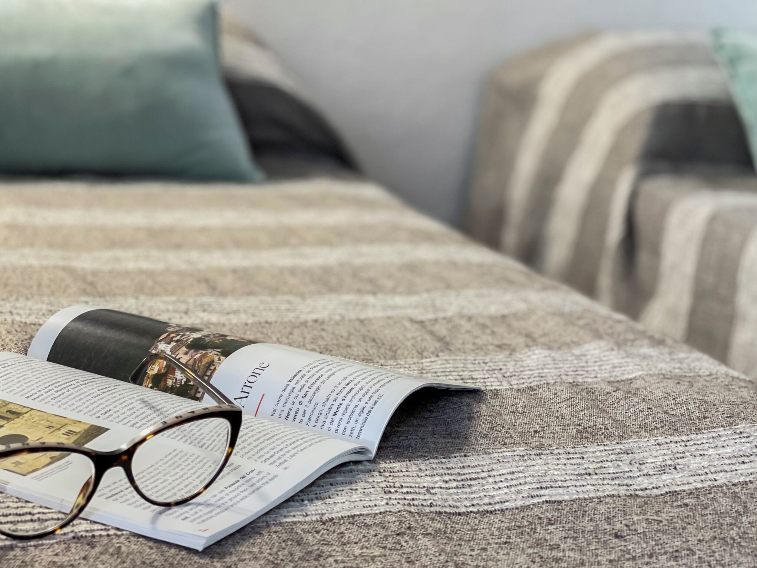 A book and glasses on a bed with striped bedding.